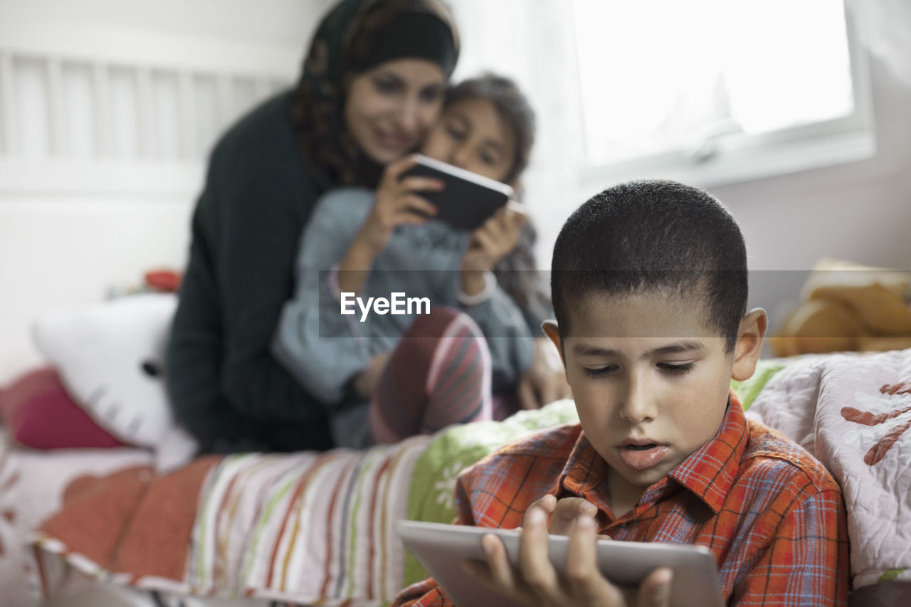 Boy using digital tablet in bedroom with family in background