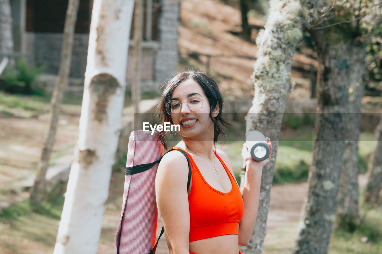 portrait of smiling young woman standing against trees