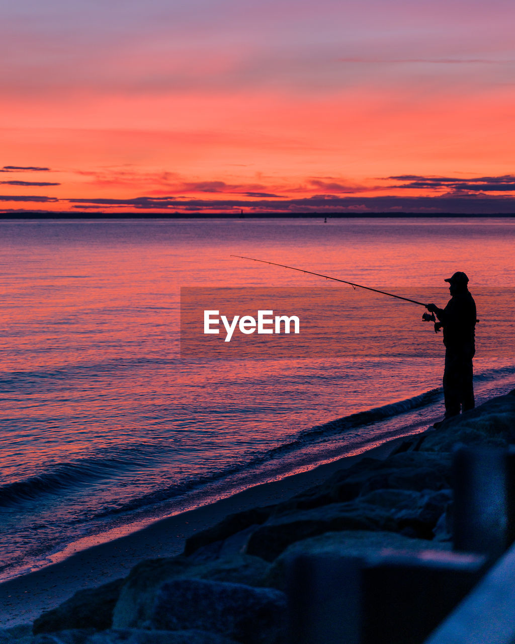 Man fishing in sea against sky during sunset