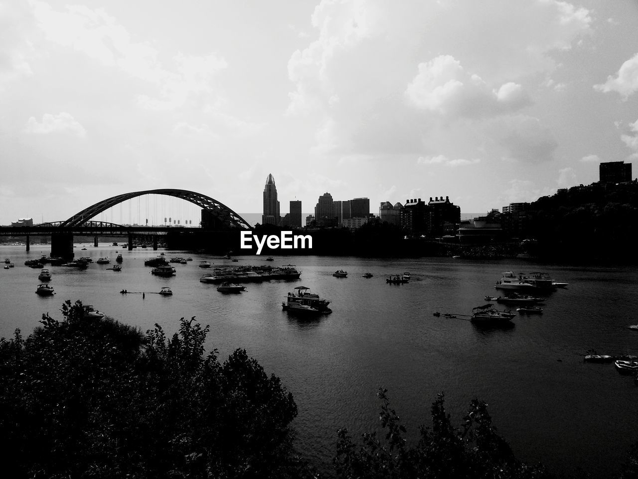 River and bridge by buildings against cloudy sky in city