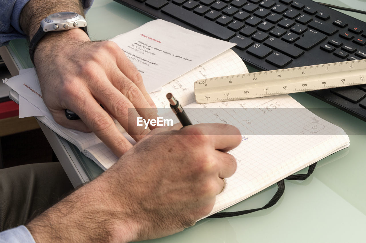 Cropped image of businessman writing in notebook at desk in office