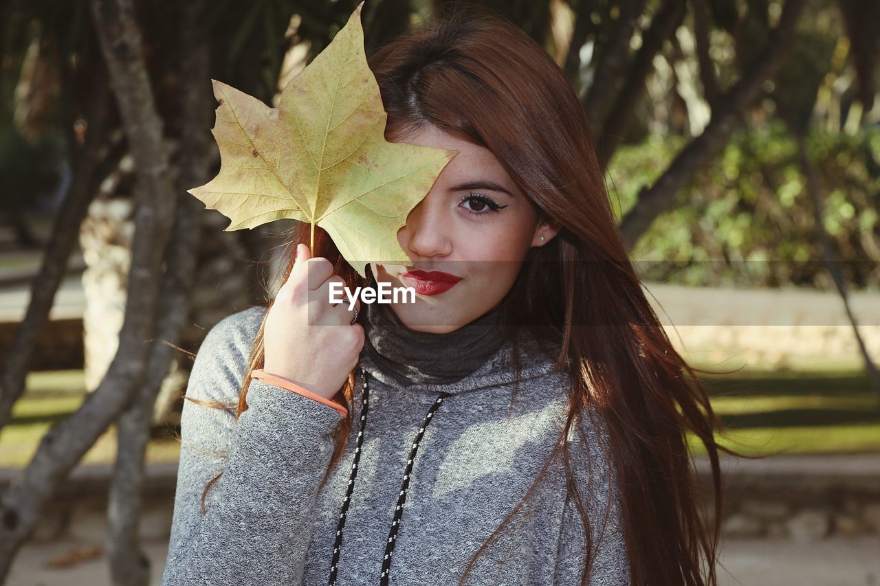 Close-up portrait of smiling young woman holding leaf