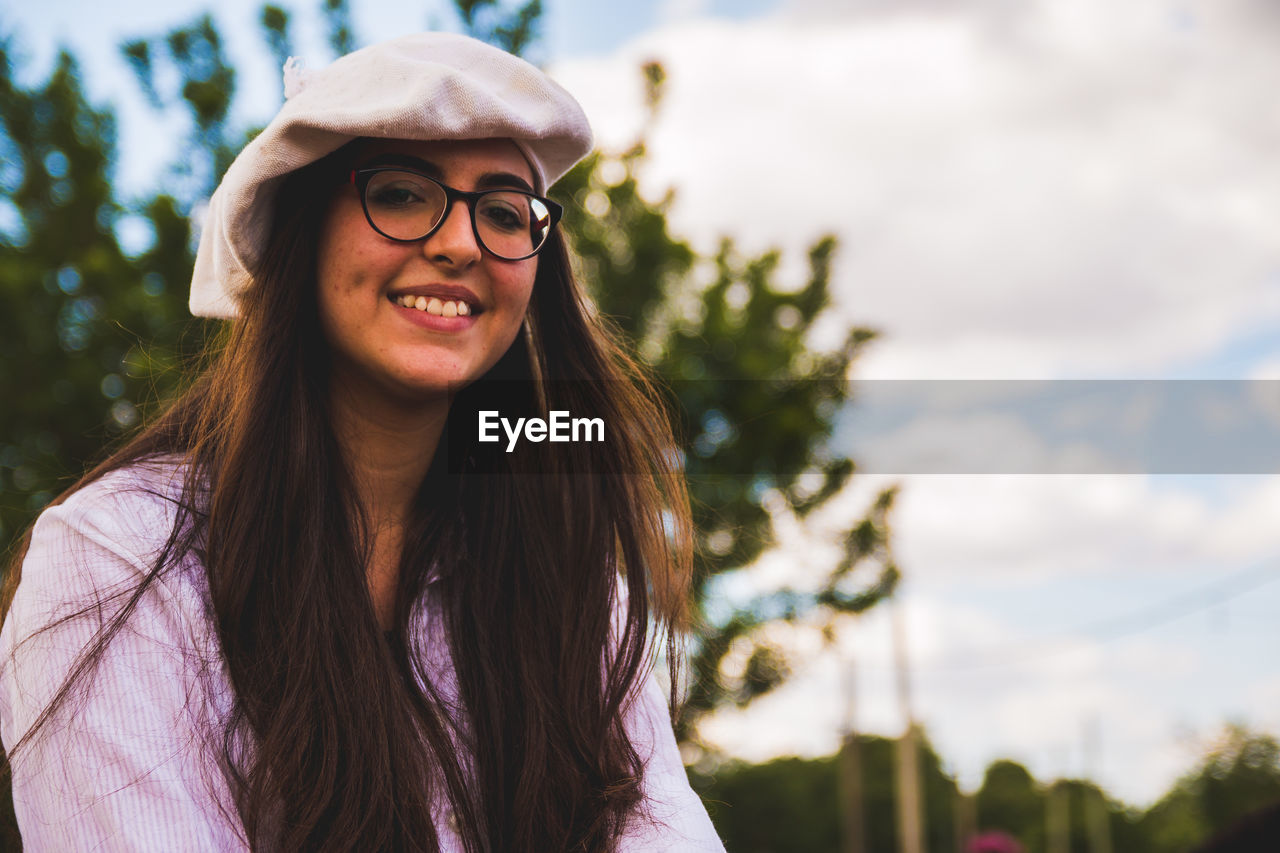 Portrait of smiling teenager girl sitting against tree