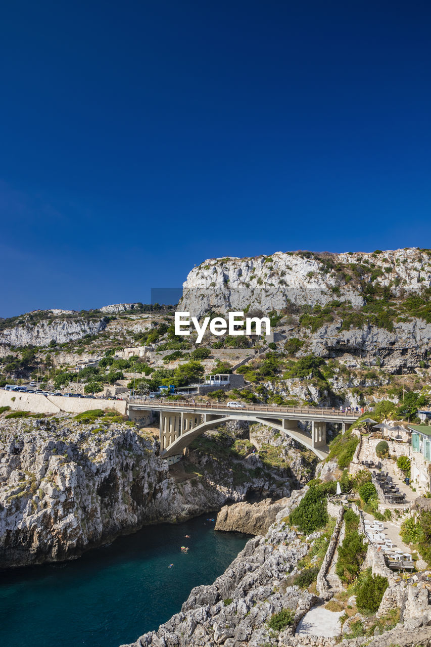 water, sky, sea, blue, coast, nature, architecture, clear sky, travel destinations, scenics - nature, land, travel, built structure, environment, rock, landscape, beauty in nature, no people, cliff, mountain, tourism, sunny, vacation, outdoors, terrain, day, tranquility, beach, building exterior, copy space, shore, non-urban scene, tranquil scene, building, plant, history, tree, rock formation, coastline, transportation, sunlight