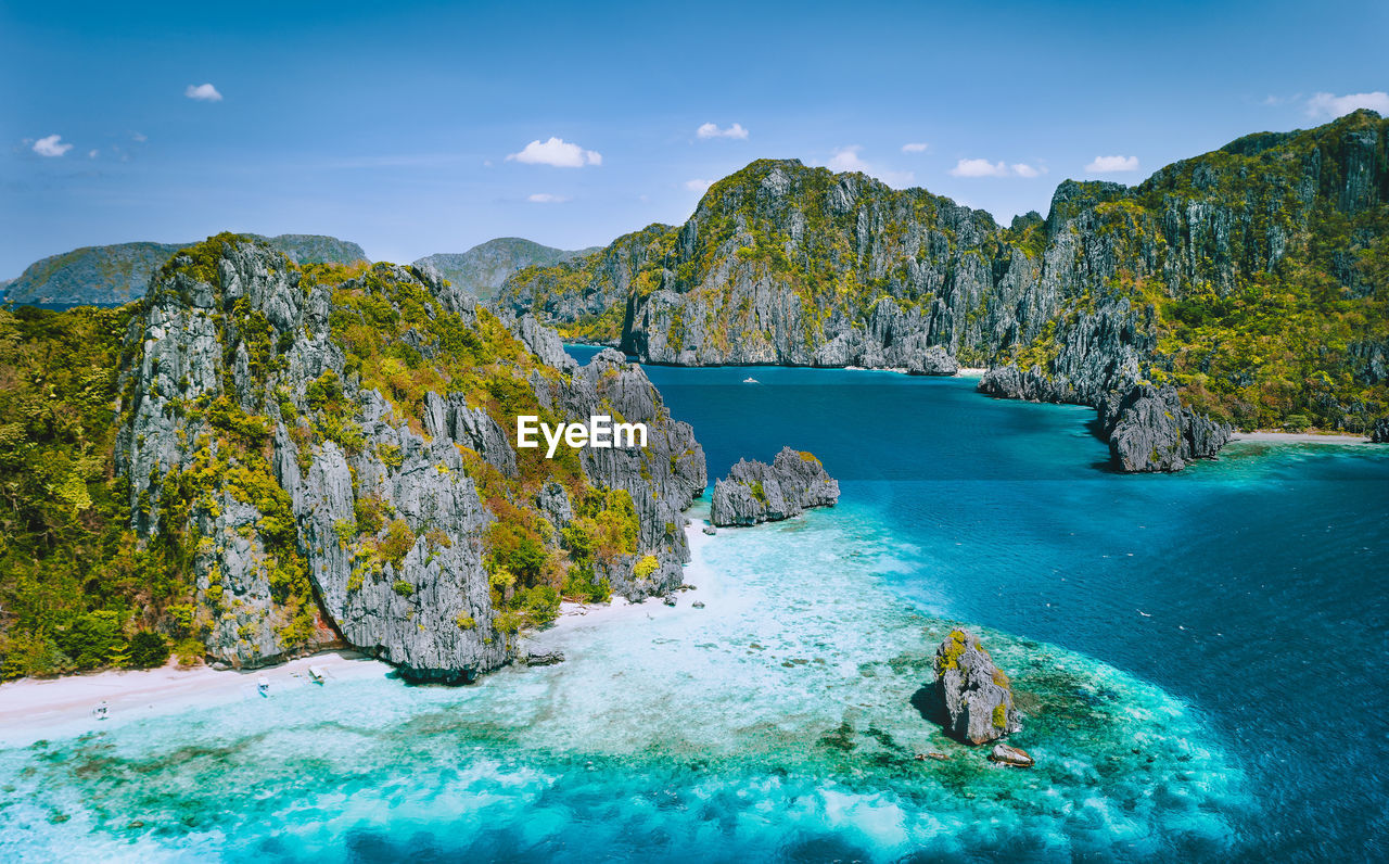 Scenic view of sea by mountain against blue sky