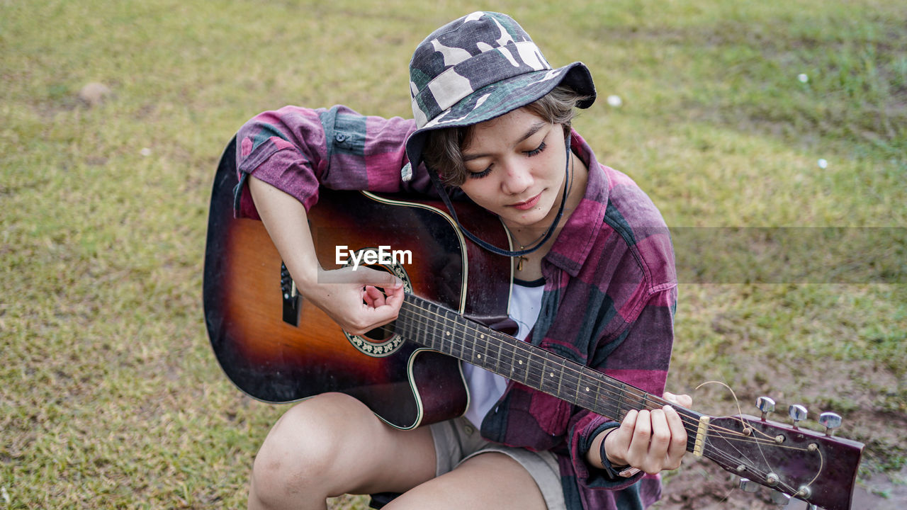 Woman playing guitar while sitting on grassy land