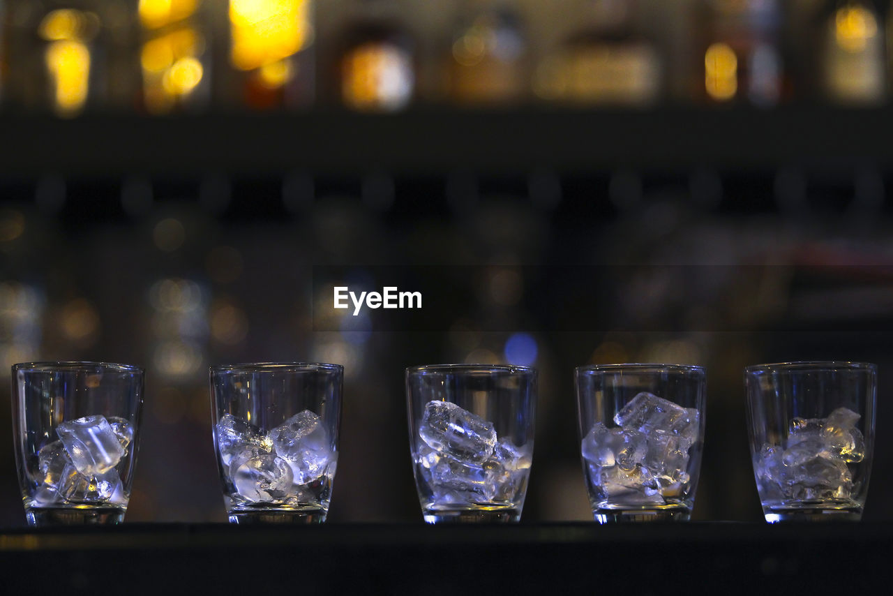 CLOSE-UP OF WINE GLASS ON TABLE AGAINST ILLUMINATED BAR