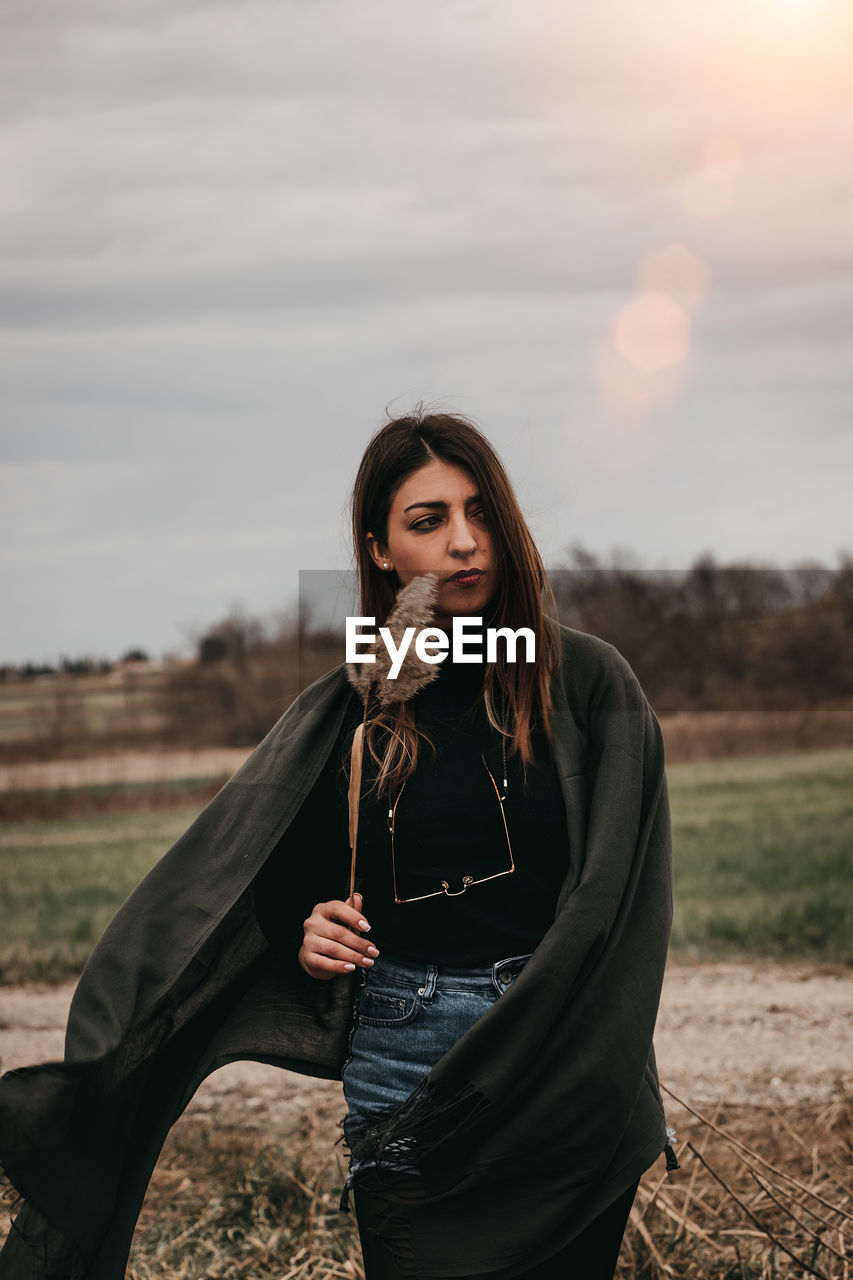 Portrait of beautiful woman standing on field against sky