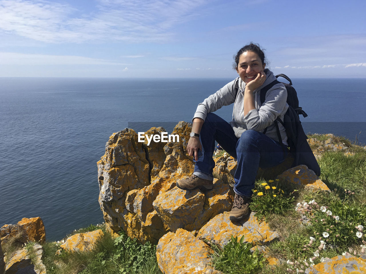 Portrait of female hiker smiling while sitting on cliff against sea