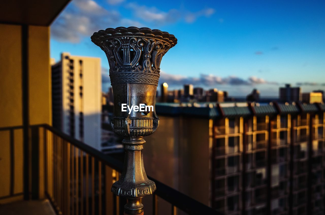 Close-up of old brass light fixture with metal railing against buildings