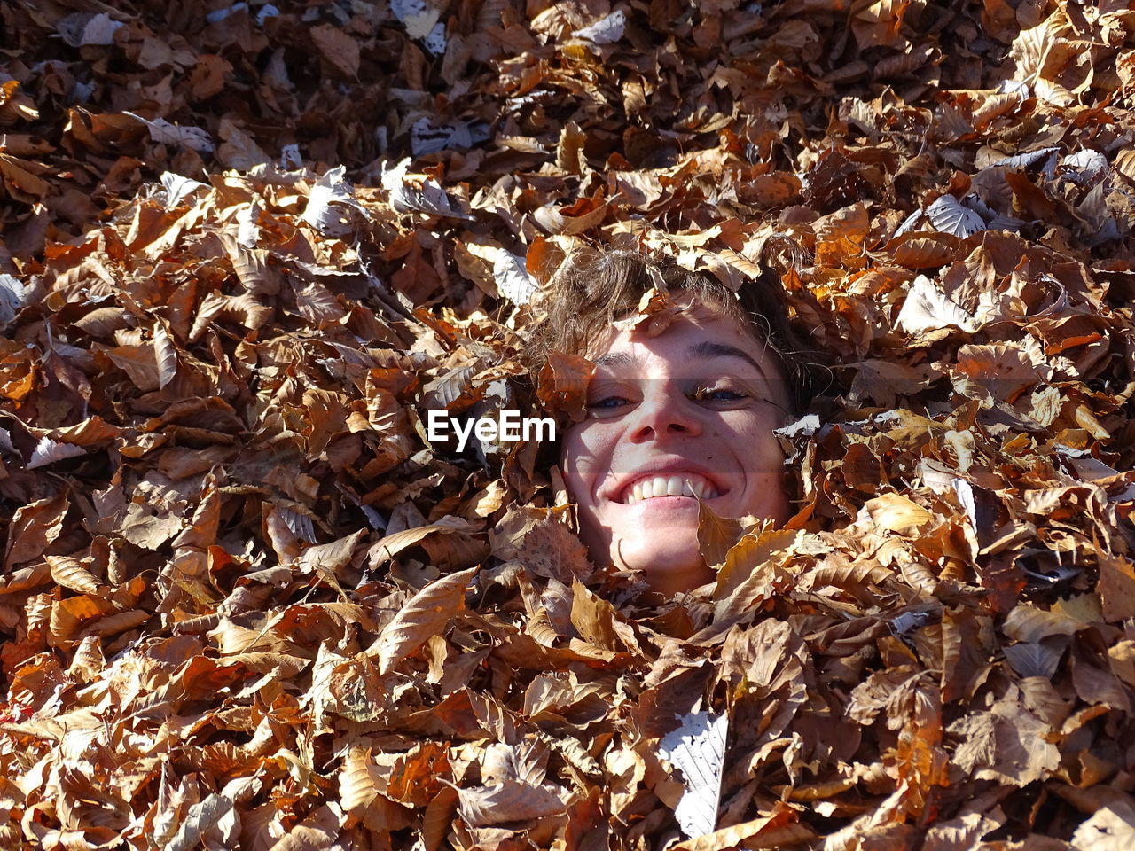 Close-up of young woman covered with dry leaves