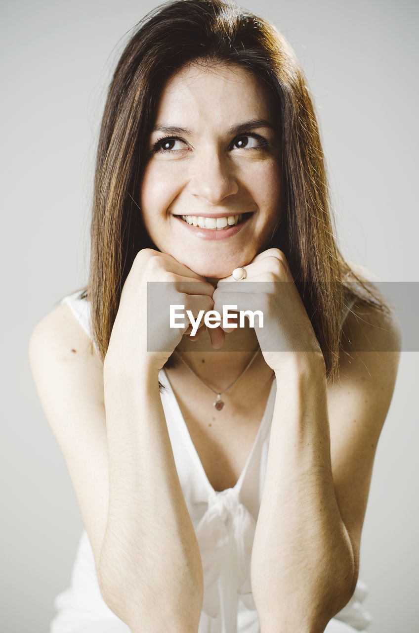 Thoughtful young woman leaning on elbows against gray background