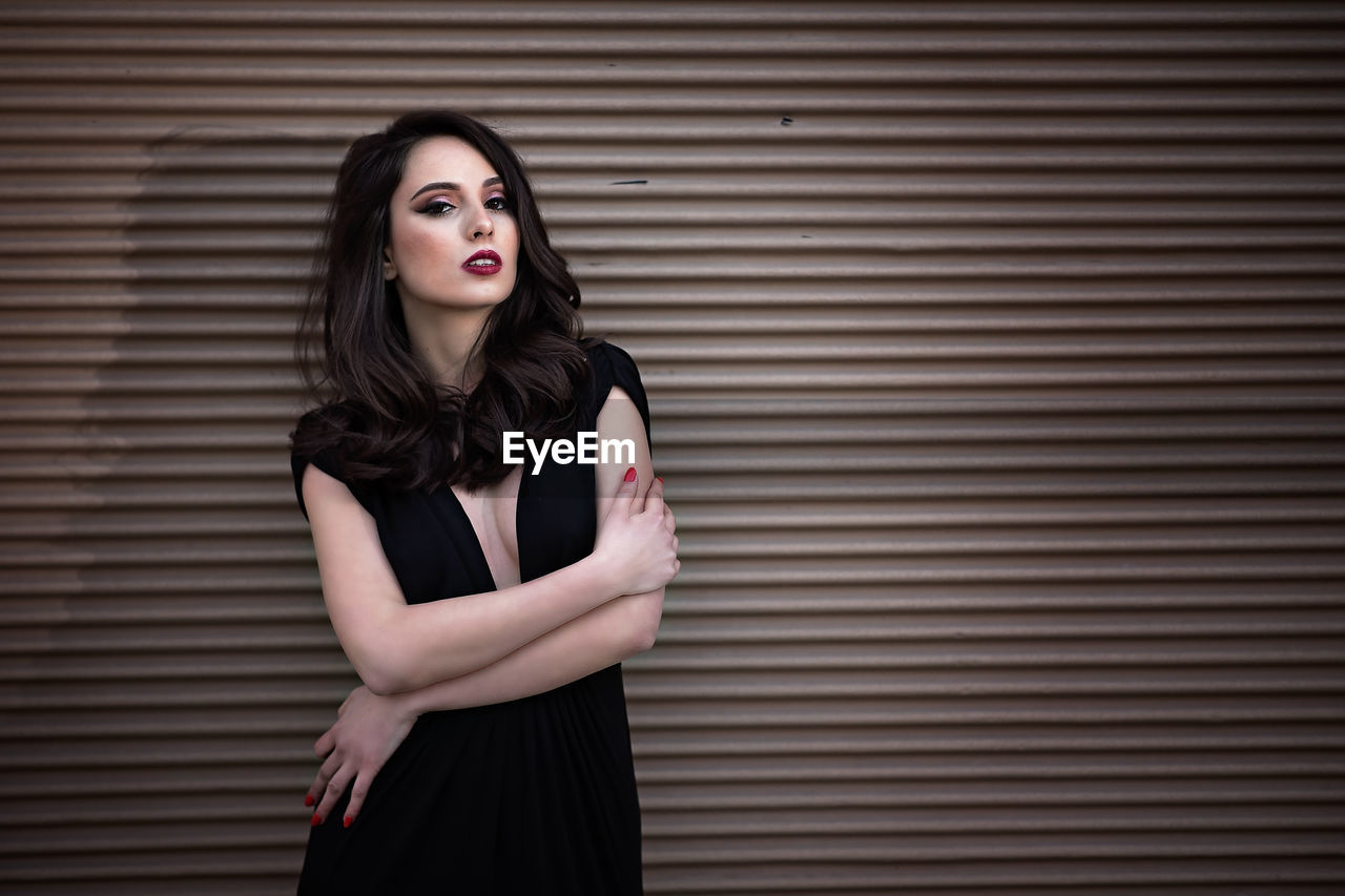 Portrait of beautiful young woman standing against shutter