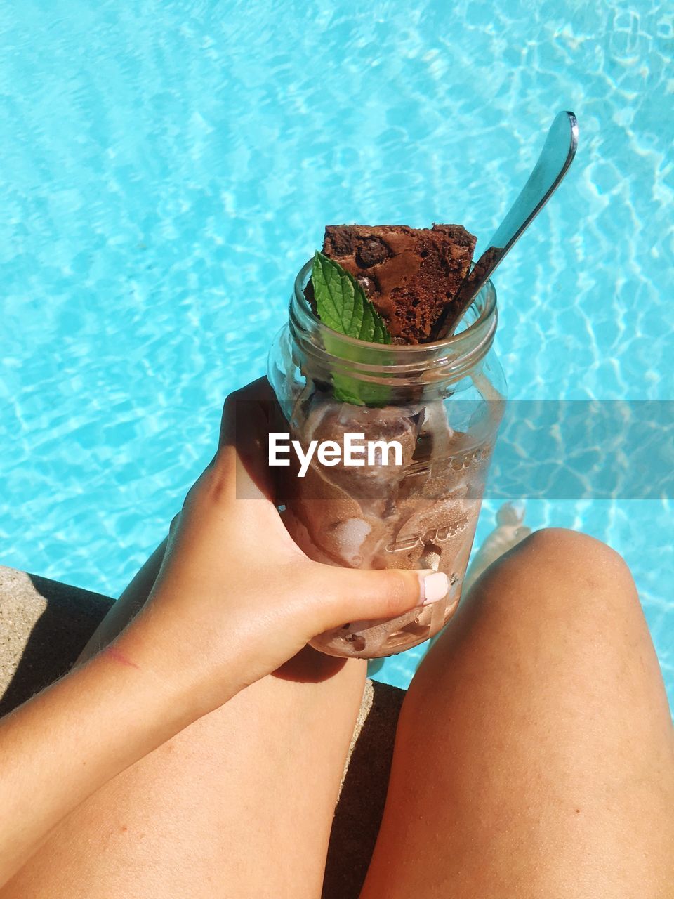 Low section of woman holding jar with dessert at poolside on sunny day