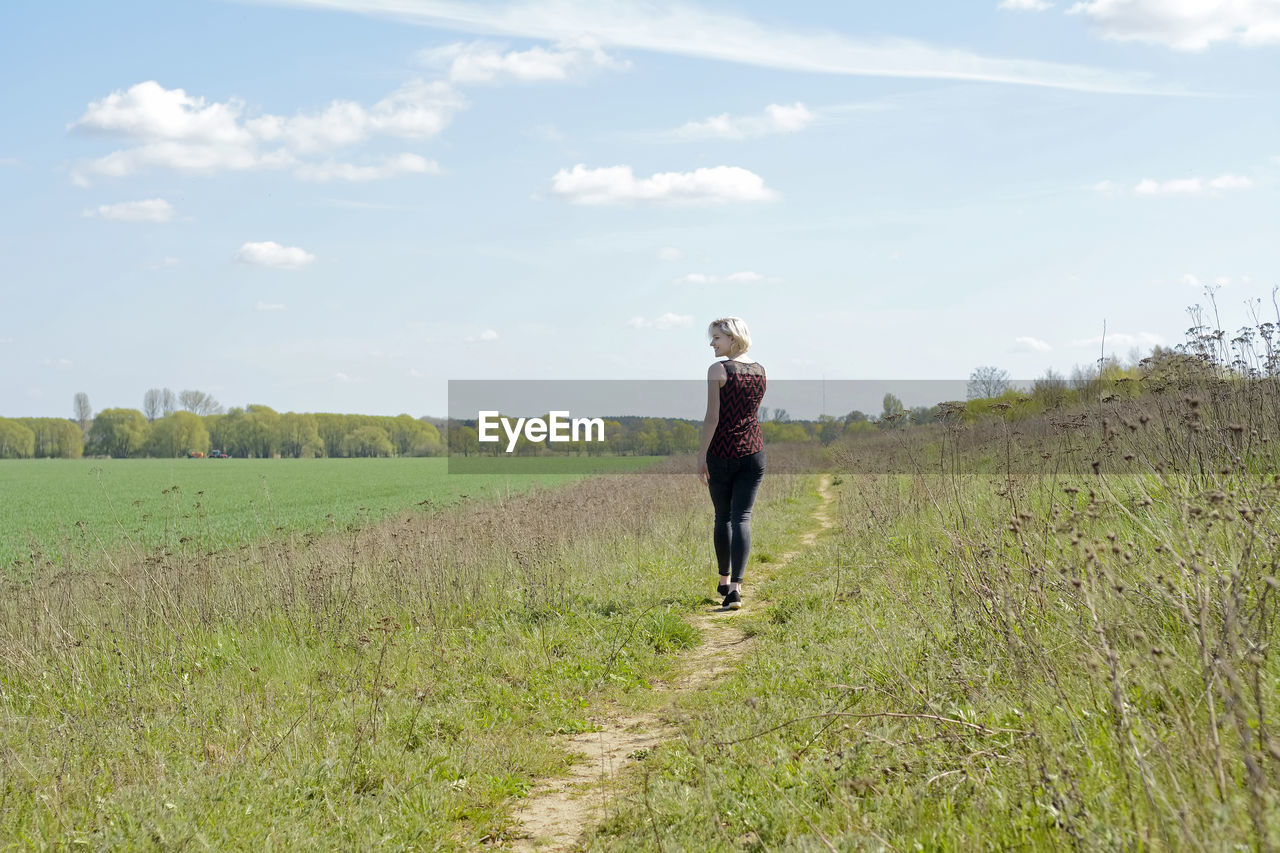 Full length rear view of woman walking on grass against sky