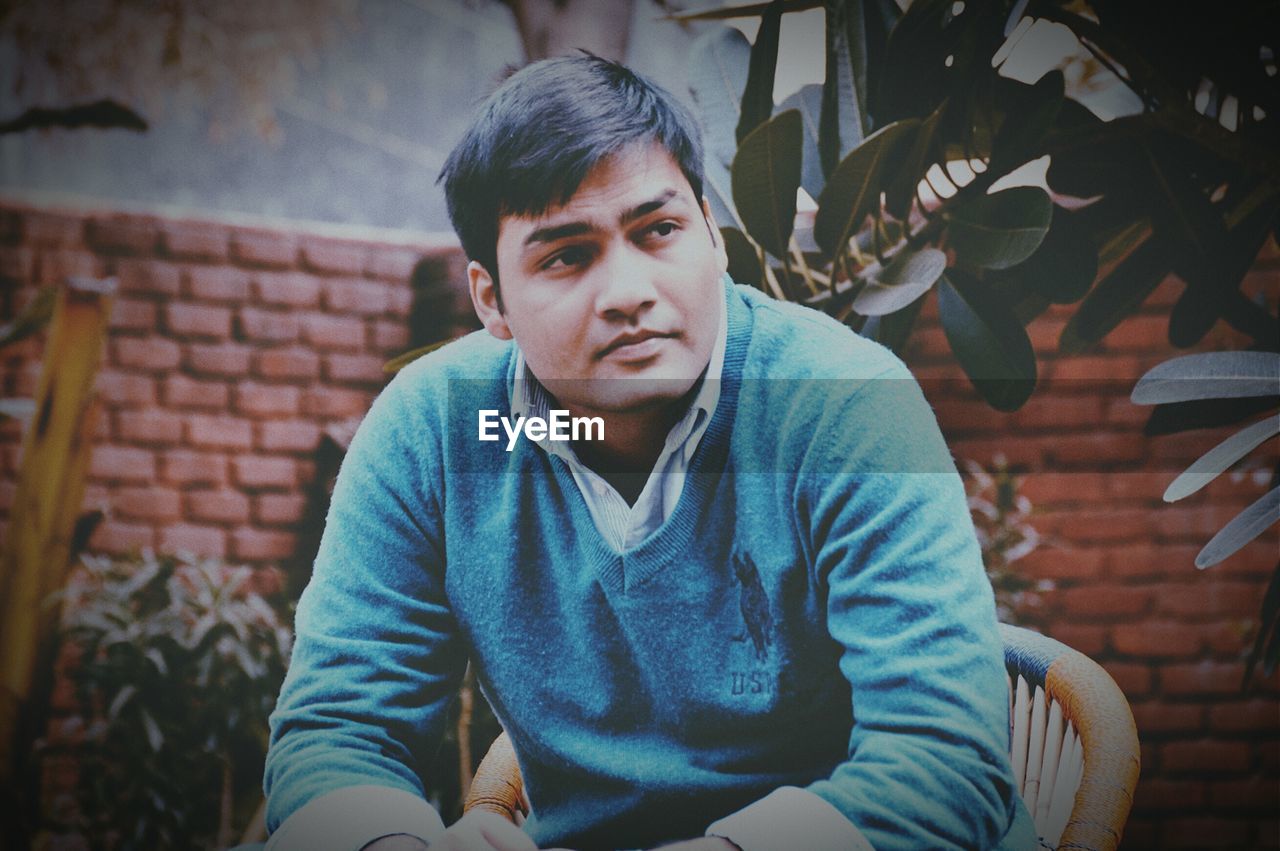 Young man looking away while sitting on chair in yard