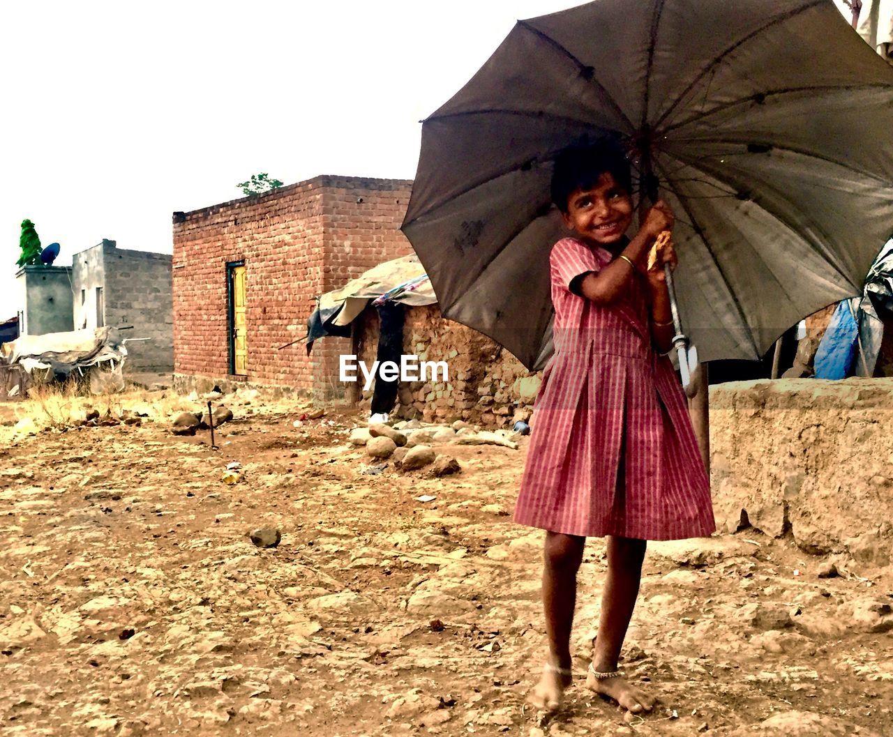 Smiling cute girl holding umbrella while standing on dirt road