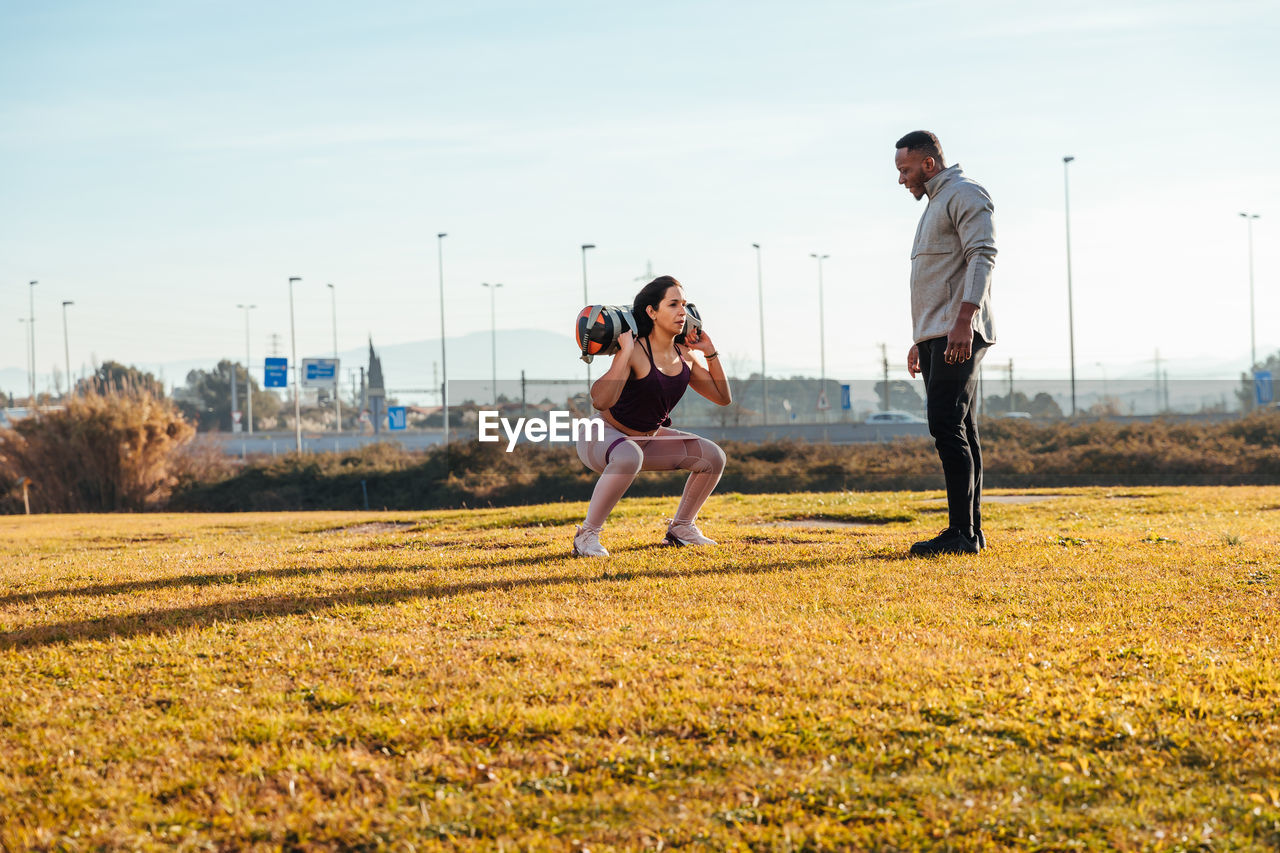 Full length of woman and man exercising on field against sky