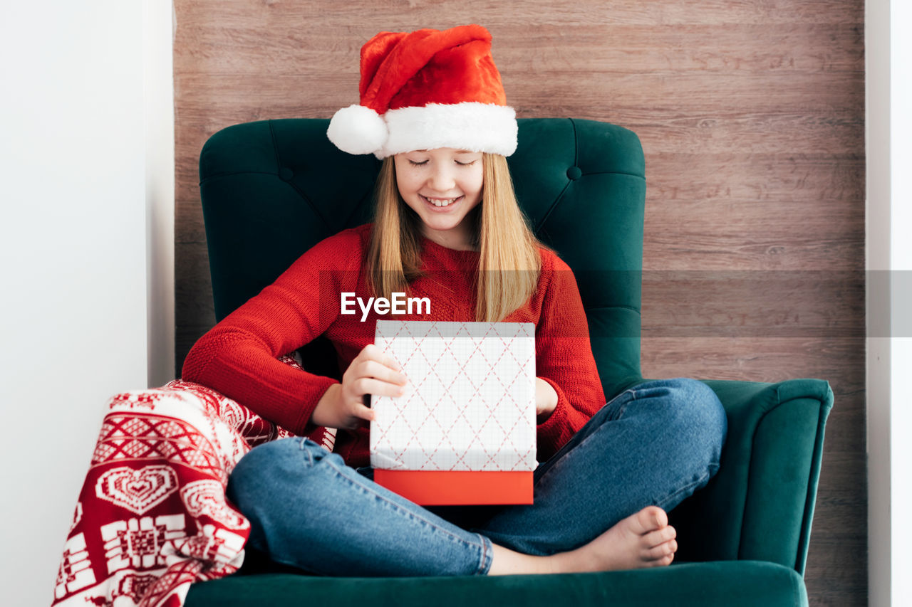 Happy smiling child girl in a christmas cap opens a christmas gift.