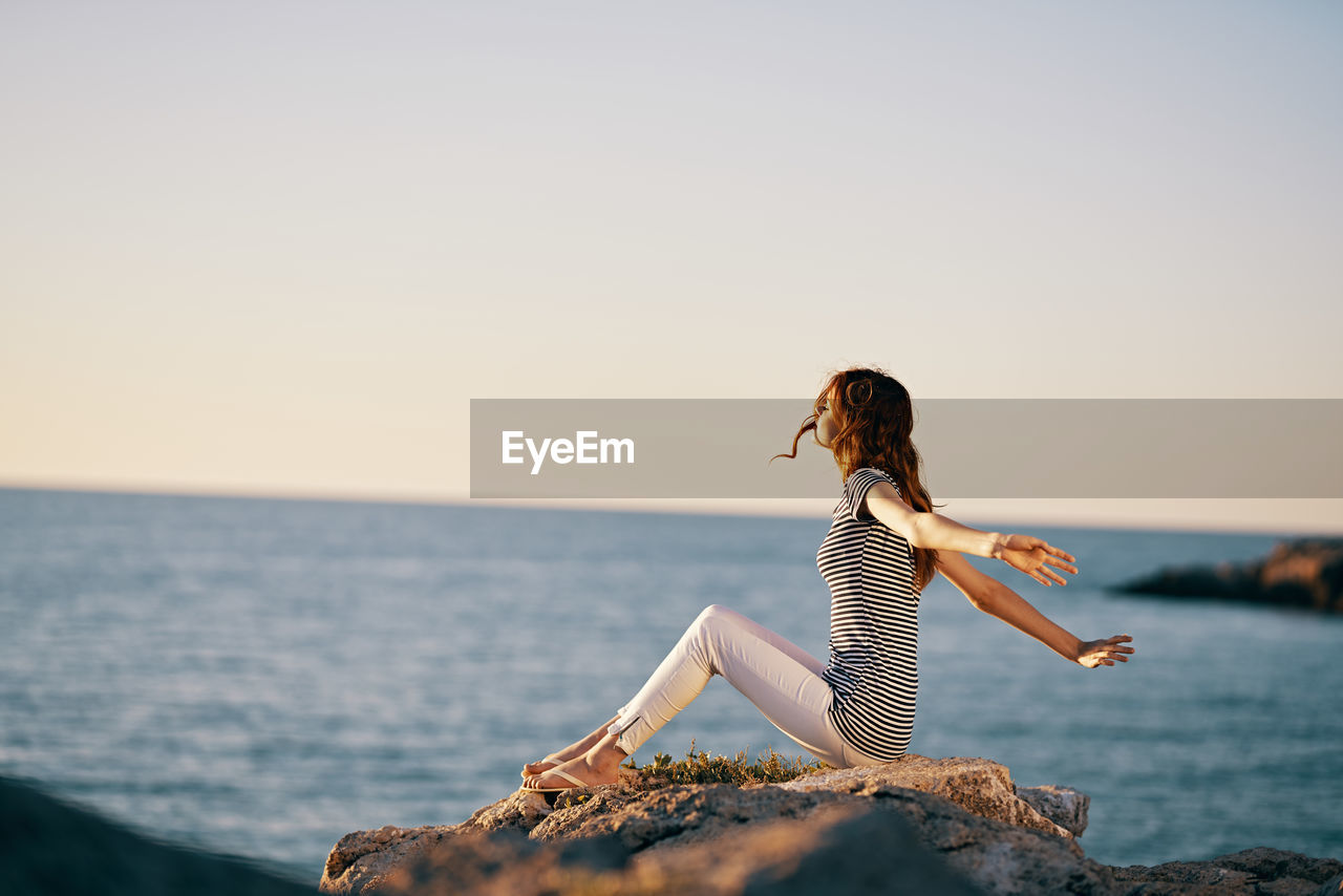 WOMAN LOOKING AT SEA AGAINST CLEAR SKY