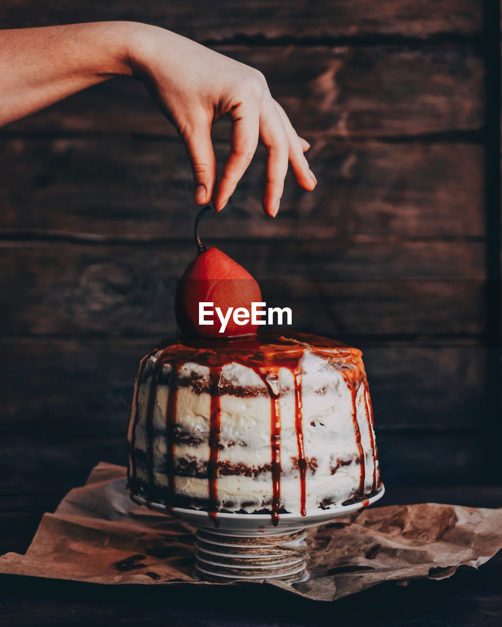 Cropped hand of person holding fruit over dessert on table