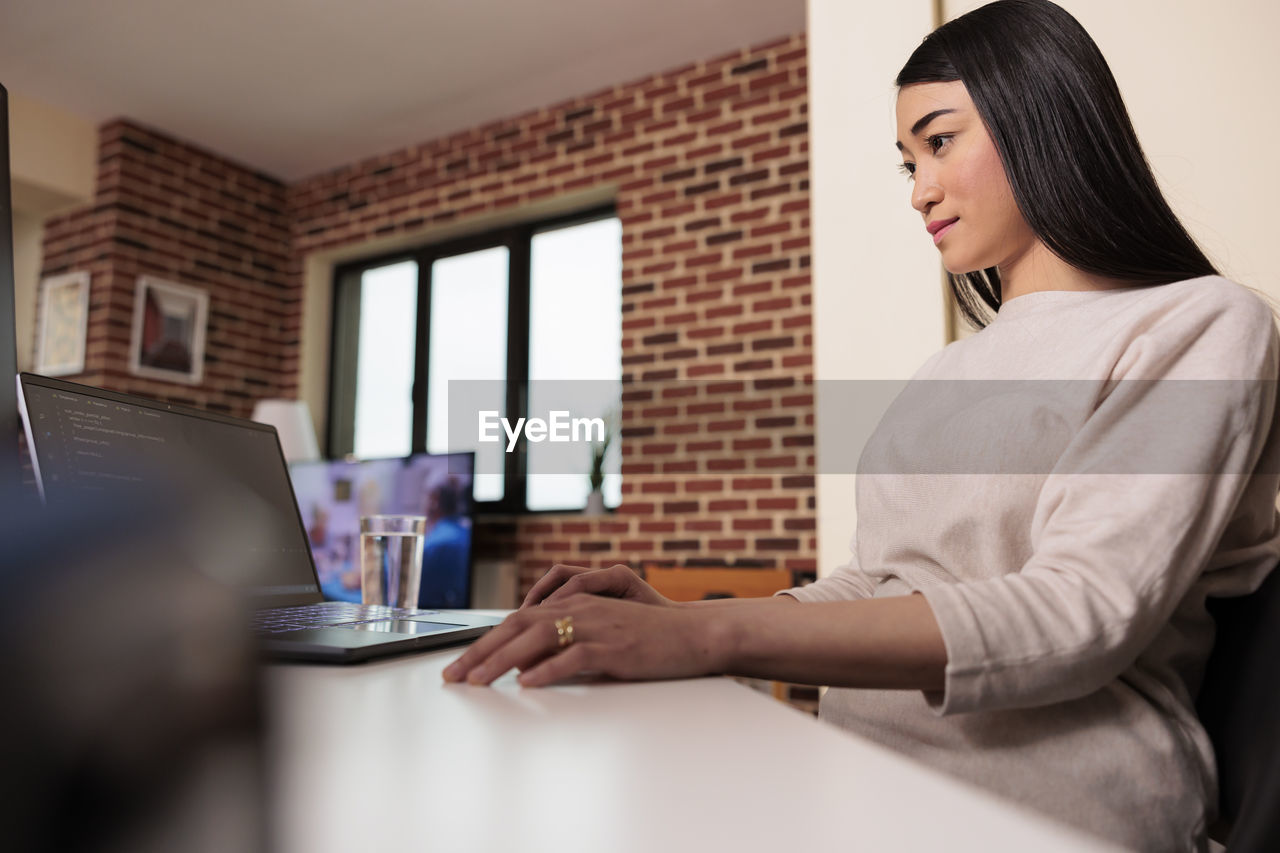 side view of young woman using laptop at home