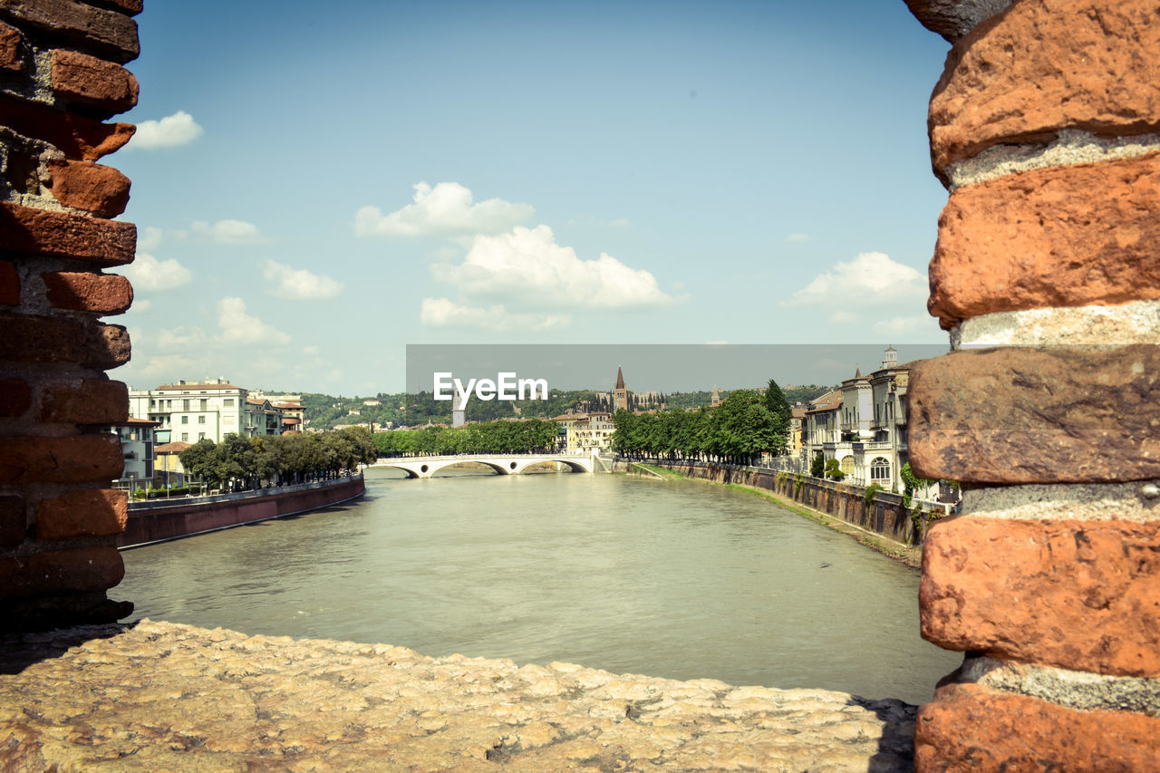 BRIDGE OVER RIVER BY BUILDINGS AGAINST SKY