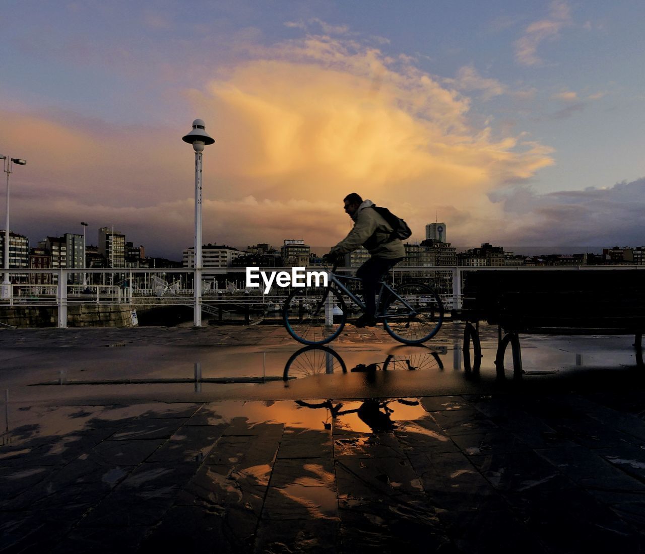 Man riding bicycle on street against sky during sunset