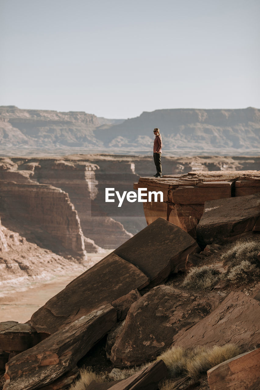 Woman stand on edge of high cliff looking over desert, hite, utah