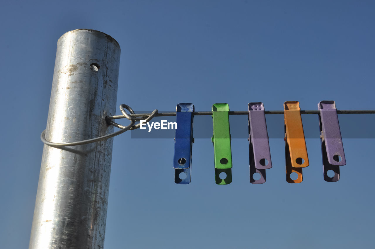 Low angle view of clothespins hanging on rope against blue sky