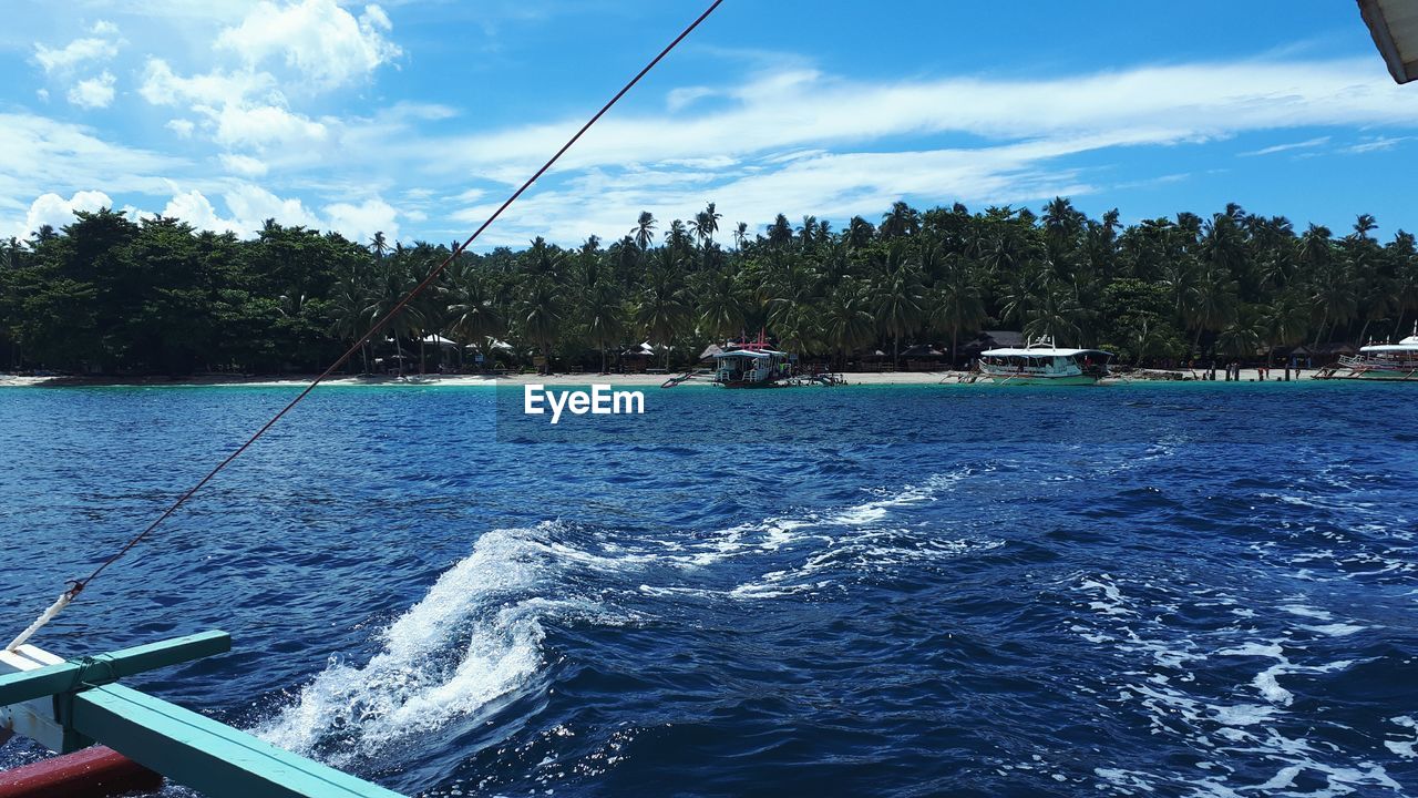 BOATS MOORED IN SEA AGAINST BLUE SKY