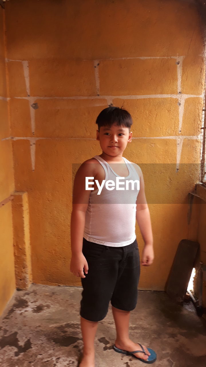 Boy looking away while standing against orange wall