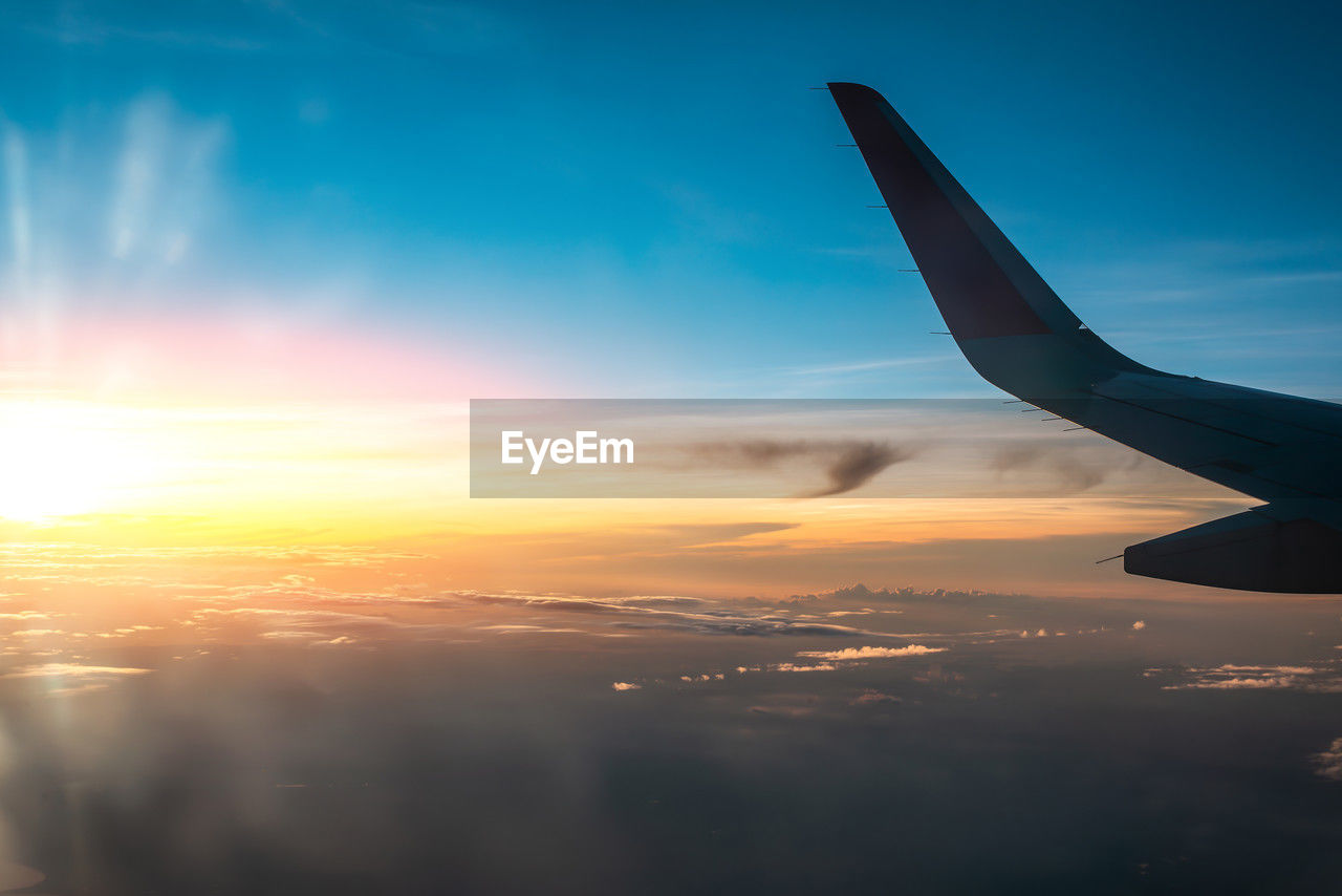 sky, airplane, aircraft wing, air vehicle, cloud, flying, transportation, sunset, travel, mode of transportation, aerial view, horizon, nature, cloudscape, journey, sunlight, blue, aircraft, no people, mid-air, sun, environment, air travel, beauty in nature, scenics - nature, dramatic sky, reflection, outdoors, airliner, urban skyline, dawn, landscape, window, vehicle, travel destinations, tranquil scene, copy space, tranquility, high up, idyllic, vacation, business travel, aviation, trip, holiday, business, motion