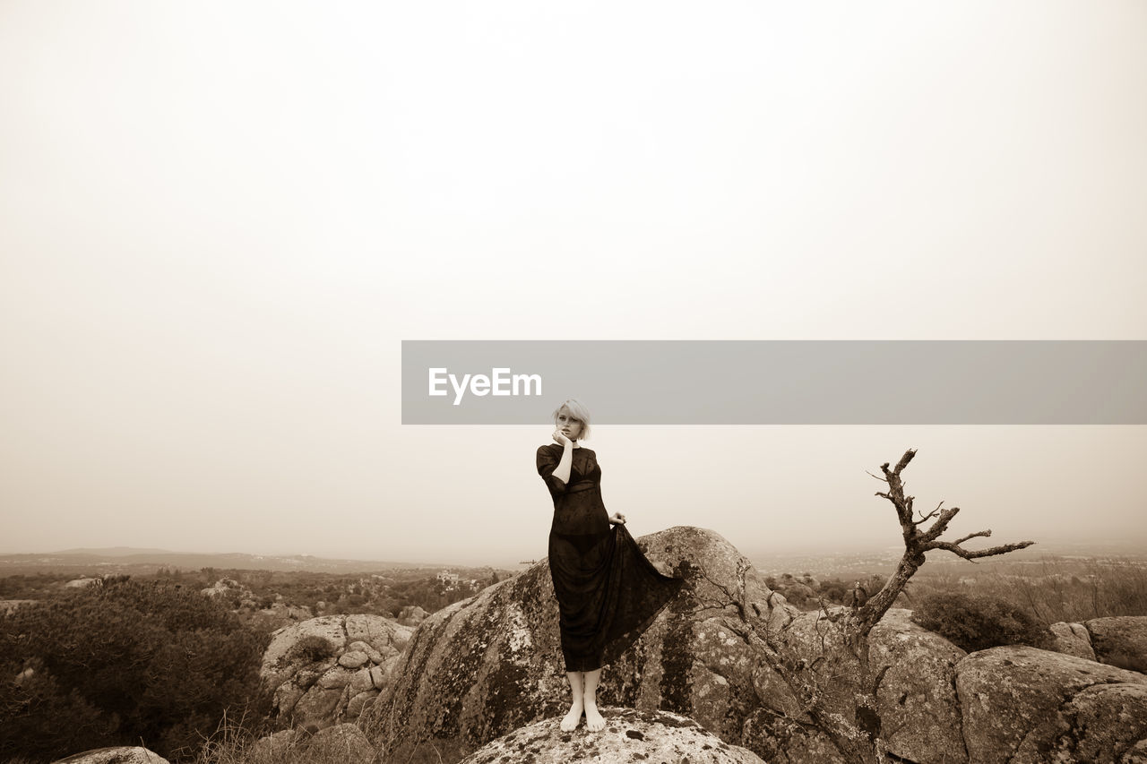 Woman standing on rock against clear sky