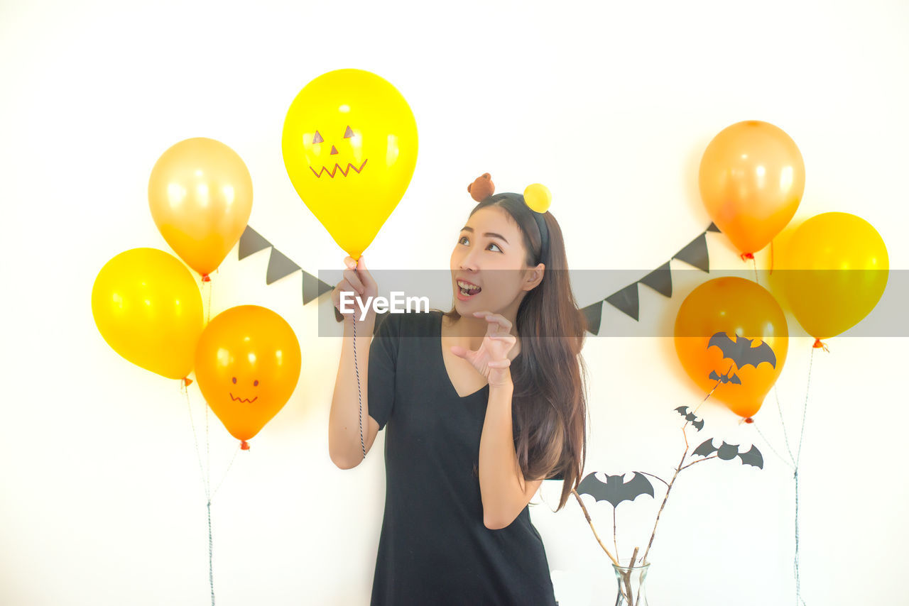 Woman holding yellow balloon against white wall during halloween