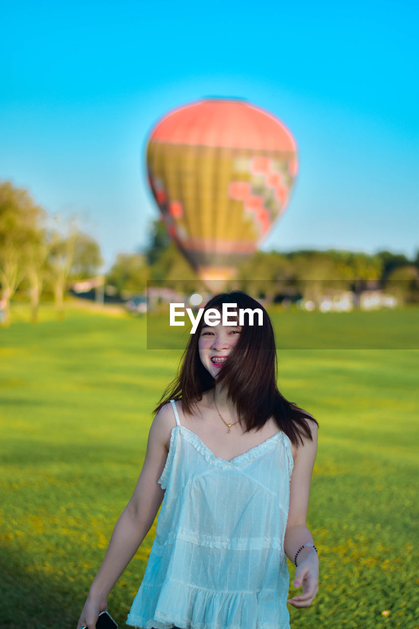 Portrait of young woman with balloons against sky