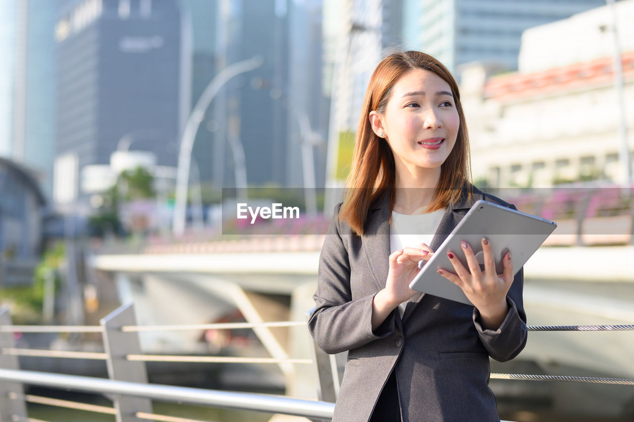 Businesswoman using digital tablet while standing in city