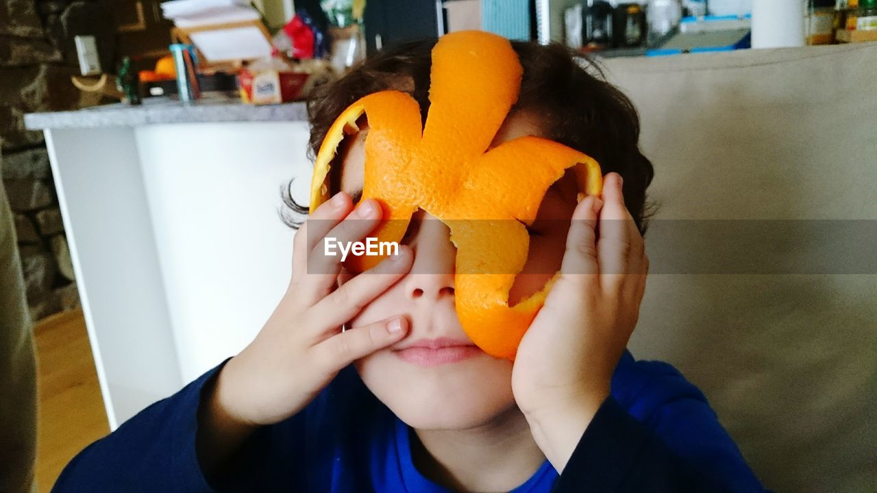 Close-up of boy playing with orange peel at home