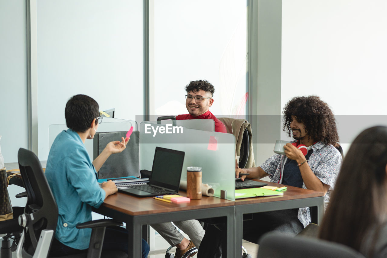 Group of positive hispanic coworkers sitting at table with laptops and communicating while working in modern office in costa rica in daylight