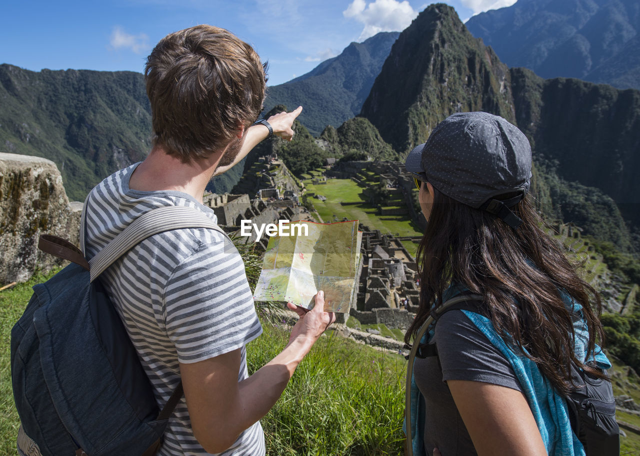 Couple at inca ruins looking at folding map, machu picchu, peru