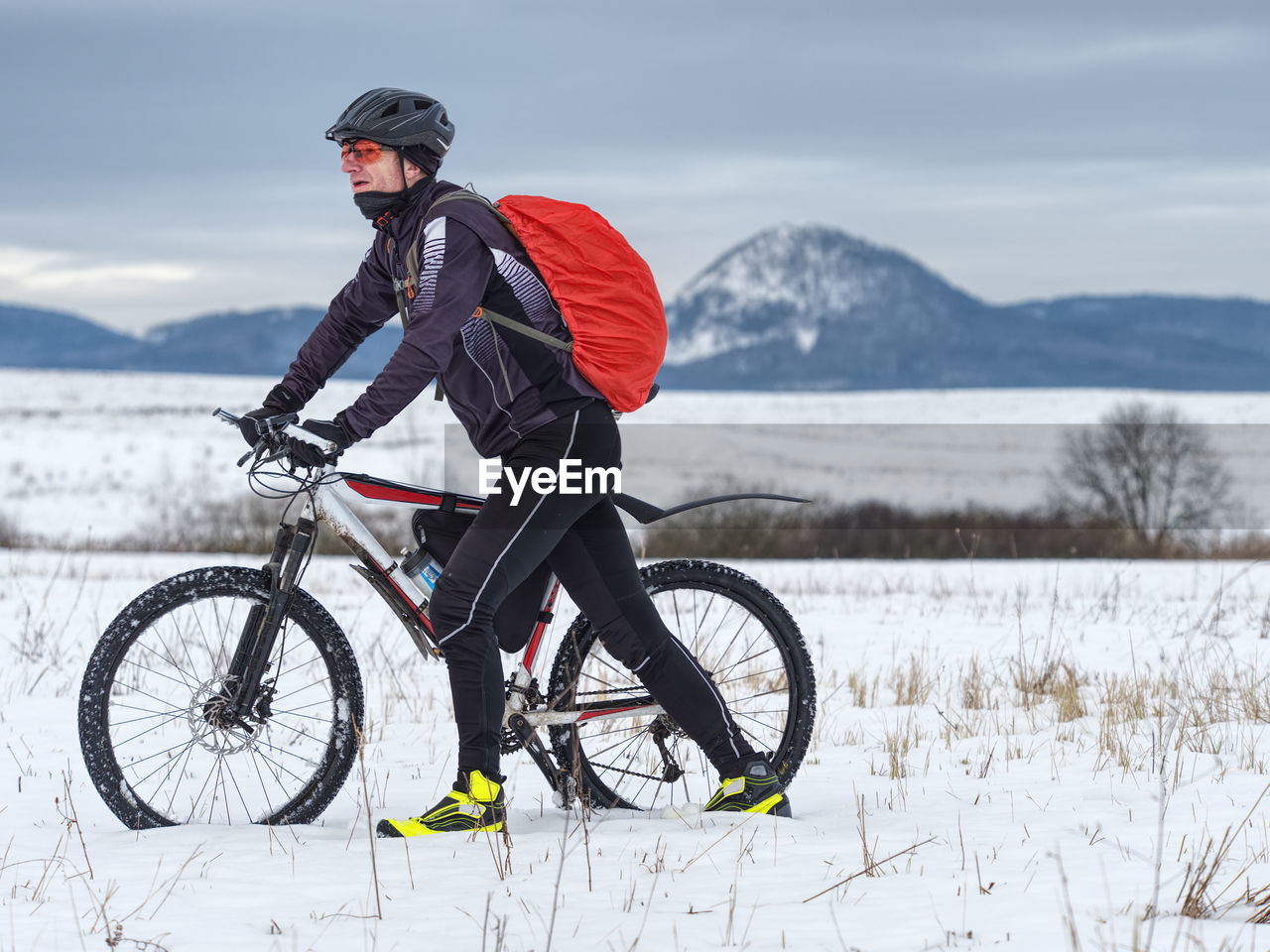 Adult biker pushes mountain bike through snow across frozen meadow. hard terrain, biker can't ride.