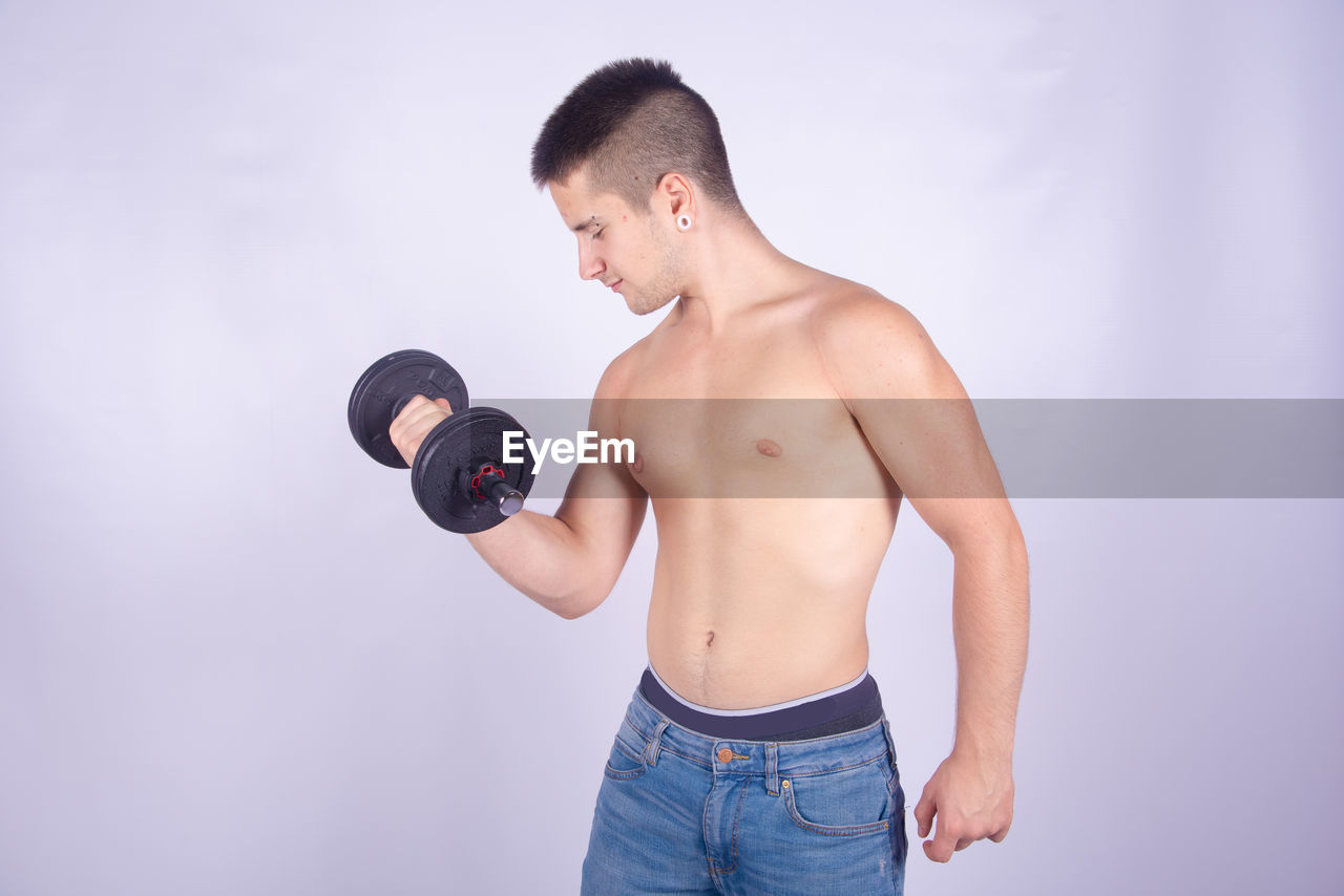 Shirtless man lifting dumbbell against purple background