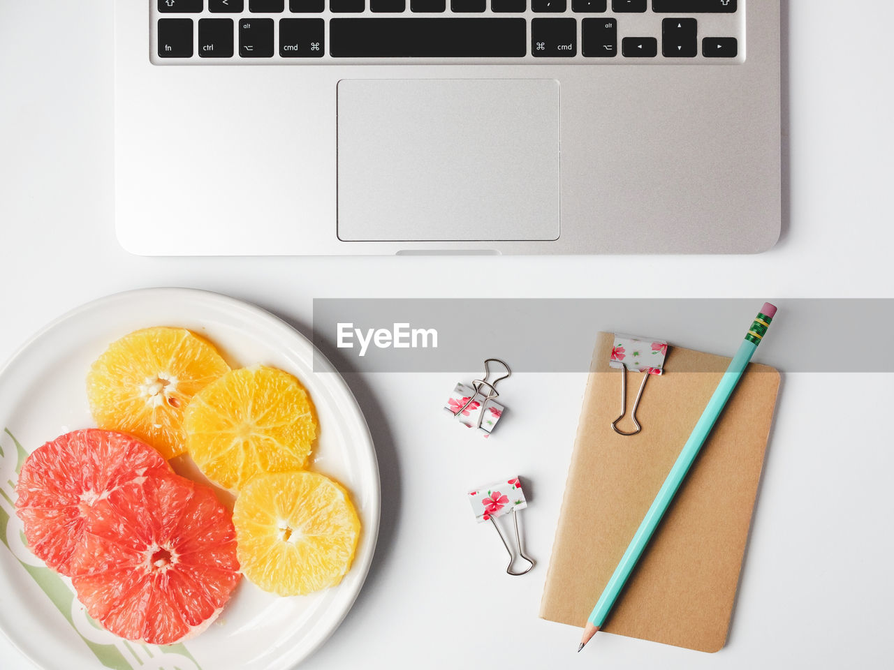 Directly above shot of citrus fruit slices in plate by laptop and diary on table