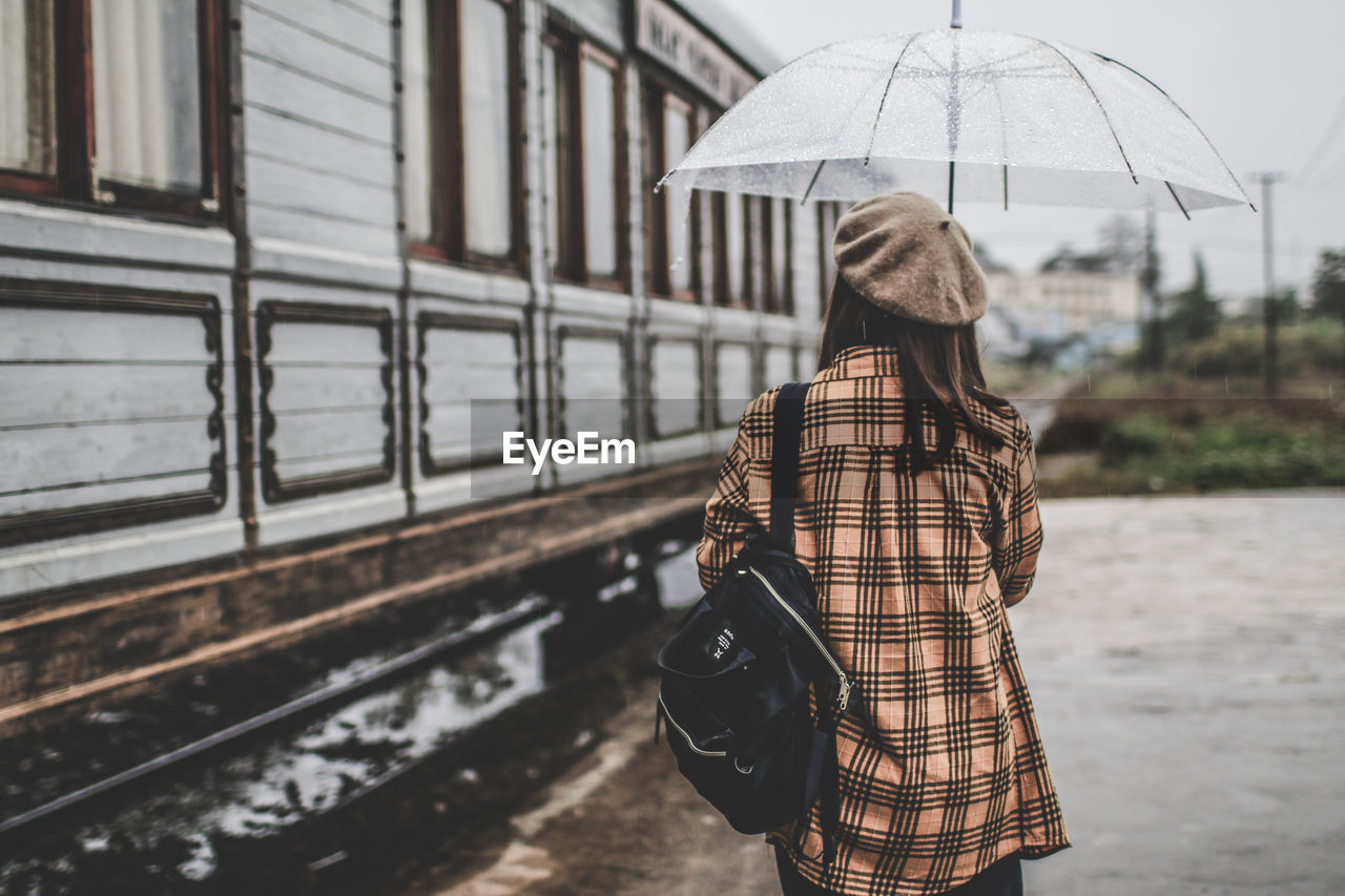 REAR VIEW OF WOMAN WITH UMBRELLA STANDING ON RAINY DAY