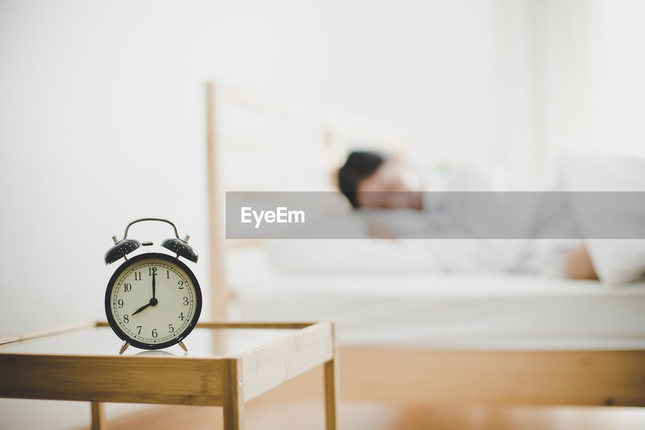 Close-up of alarm clock on side table against woman sleeping at home 