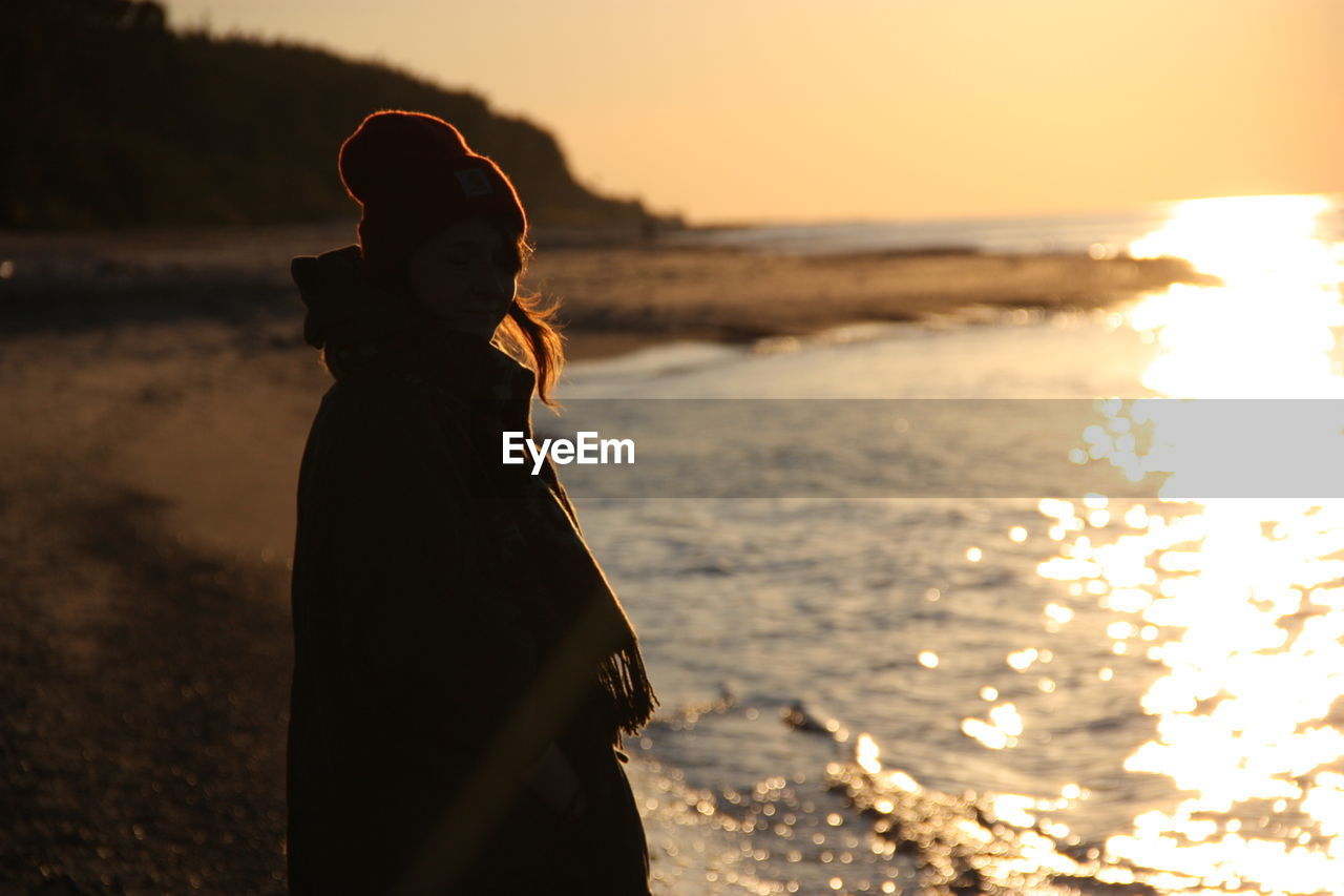 Side view of woman standing by shore during sunset