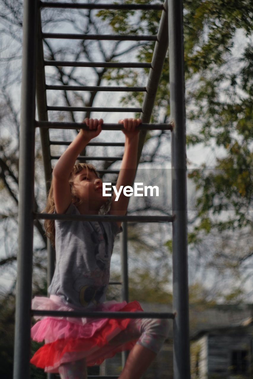 Girl climbing on monkey bars against sky