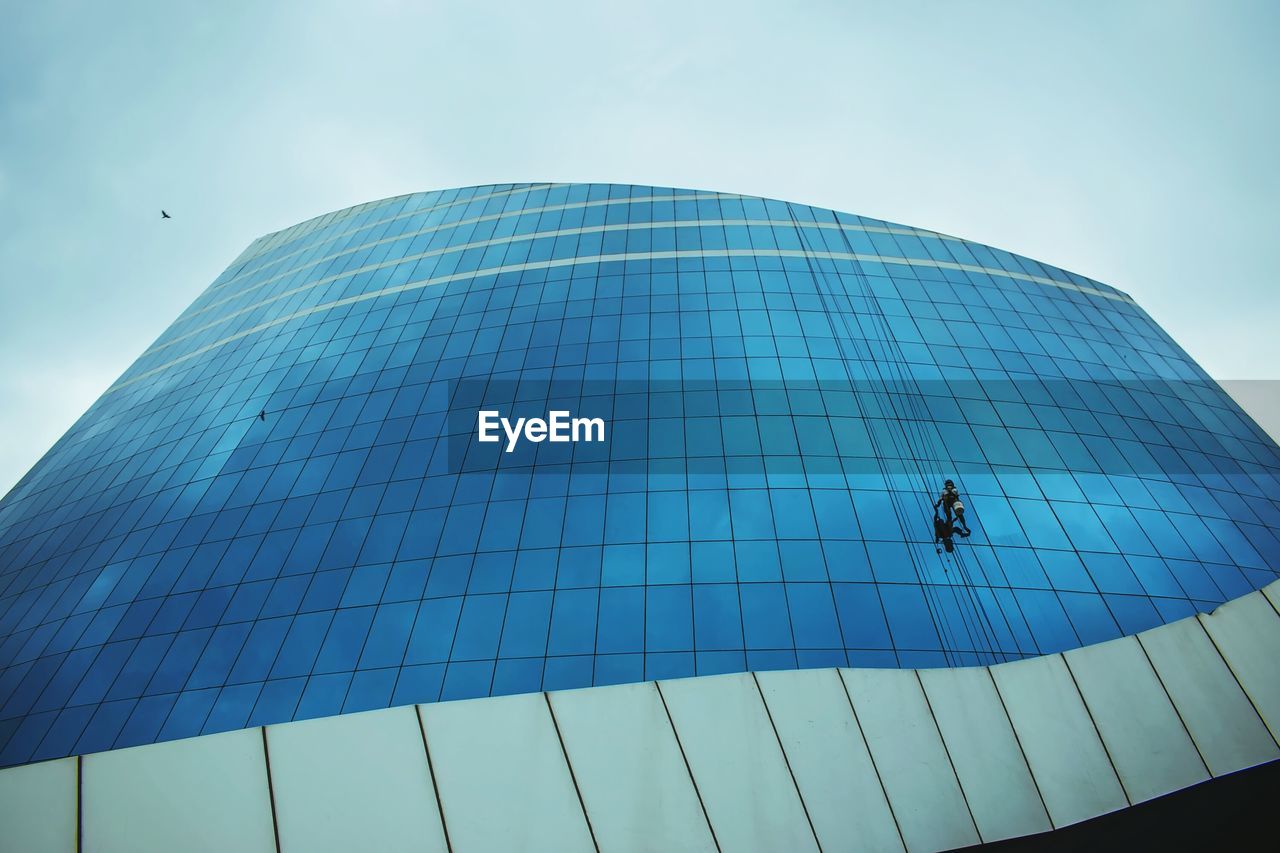 LOW ANGLE VIEW OF MODERN GLASS BUILDING AGAINST BLUE SKY