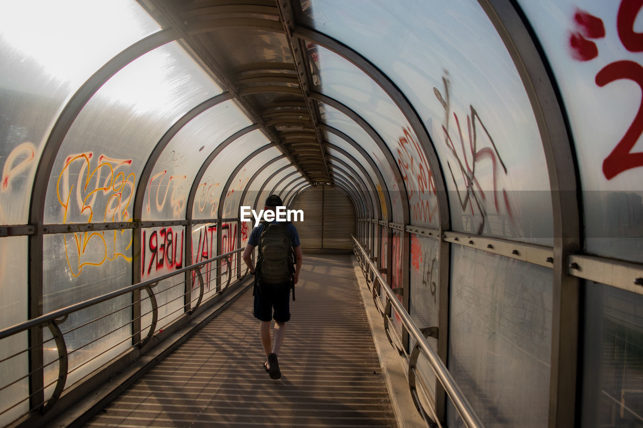Rear view of man walking on footpath in graffiti tunnel