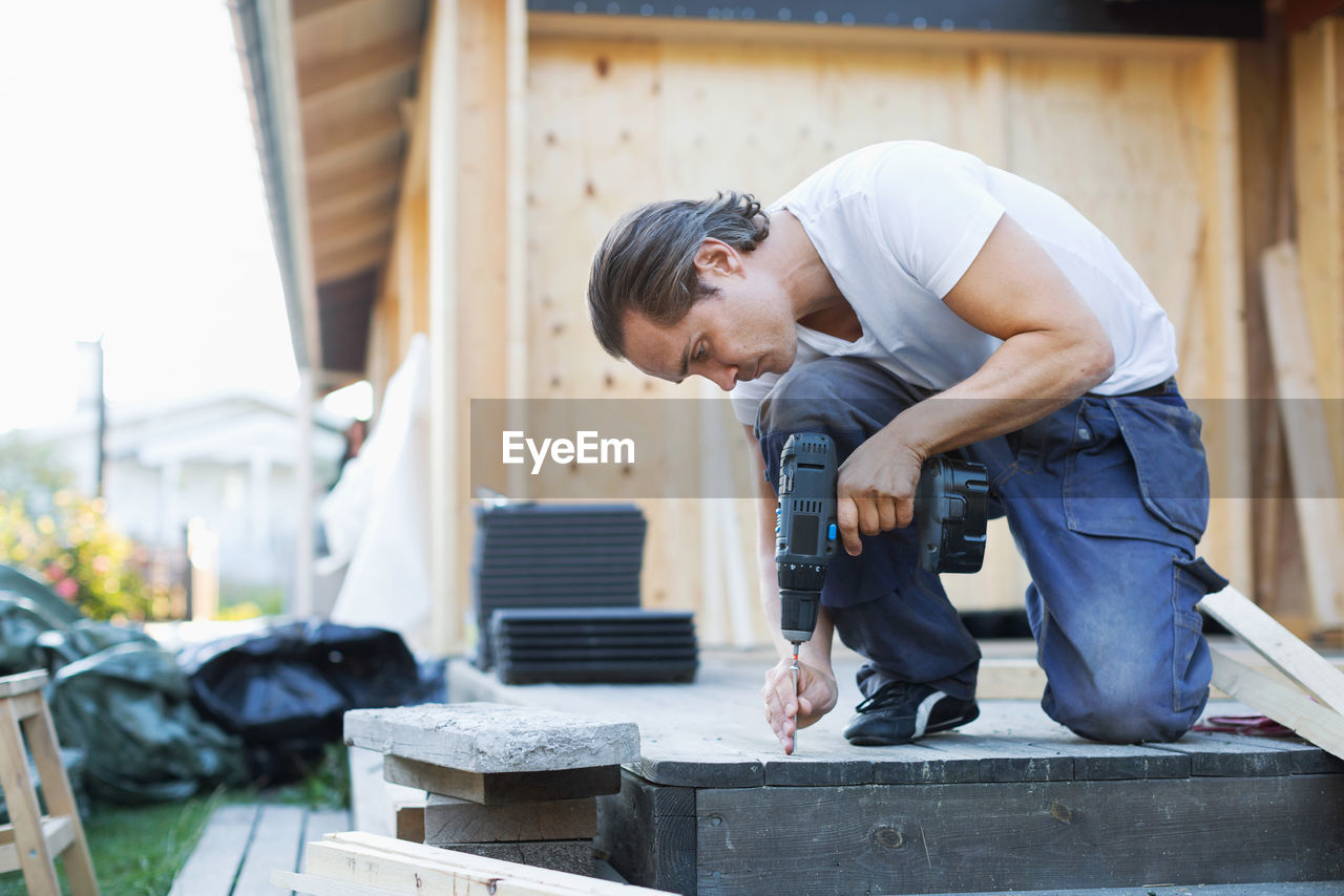 Full length of man using cordless screwdriver nail into floorboard